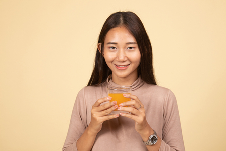 Young Asian woman drink orange juice  on beige backgroundの写真素材