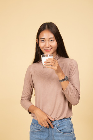 Healthy Asian woman drinking a glass of milk  on beige backgroundの写真素材