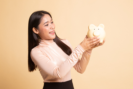 Young Asian woman with a pig coin bank on  beige backgroundの写真素材