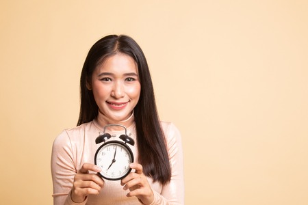 Young Asian woman smile with a clock on  beige background