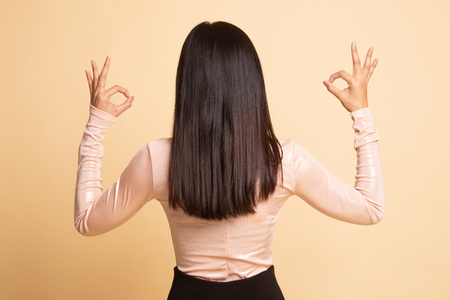 Back view of Asian woman show double OK hand sign on  beige backgroundの写真素材