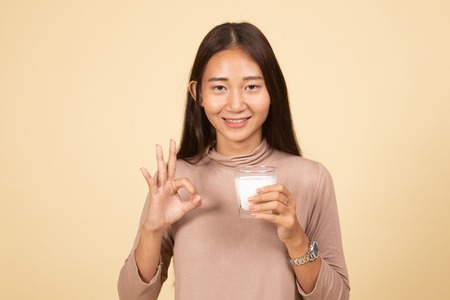 Healthy Asian woman drinking a glass of milk show OK sign  on beige backgroundの写真素材