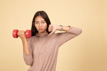 Unhappy Asian woman thumbs down with dumbbells  on beige backgroundの写真素材