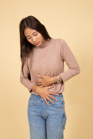 Young Asian woman got stomachache  on beige backgroundの写真素材