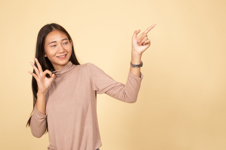 Young Asian woman point and show OK  on beige backgroundの写真素材