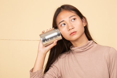 Young Asian woman with tin can phone  on beige backgroundの写真素材