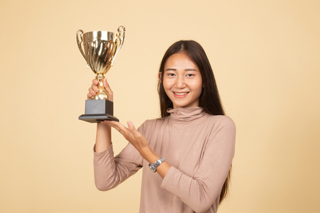 Successful young asian woman holding a trophy  on beige backgroundの写真素材