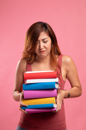 Unhappy young Asian woman studying  with may books on pink backgroundの写真素材