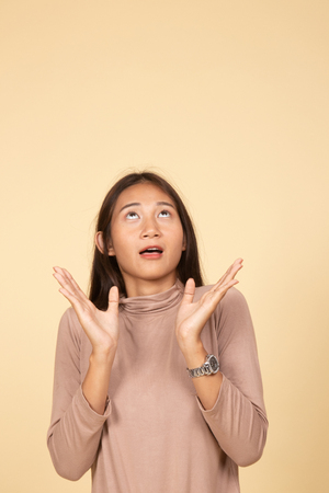 Excited young Asian woman look up  on beige backgroundの写真素材