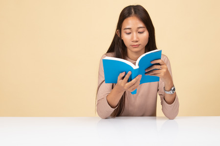 Young Asian woman read a book with cup of coffee  on beige backgroundの写真素材