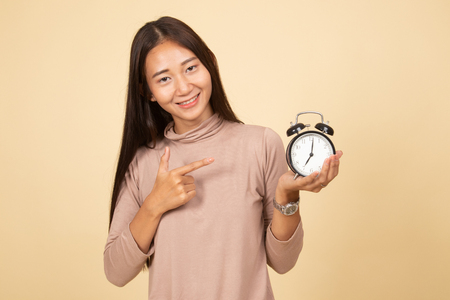 Young Asian woman point to a clock  on beige backgroundの写真素材