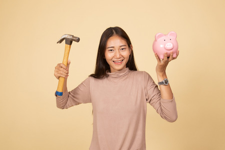 Asian woman with pig coin bank and hammer  on beige backgroundの写真素材