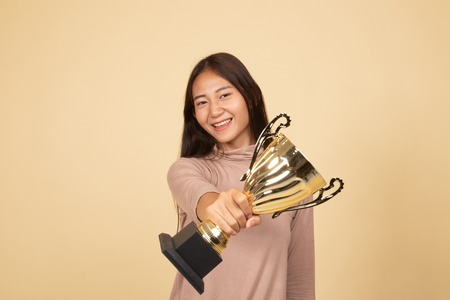 Successful young asian woman holding a trophy  on beige backgroundの写真素材