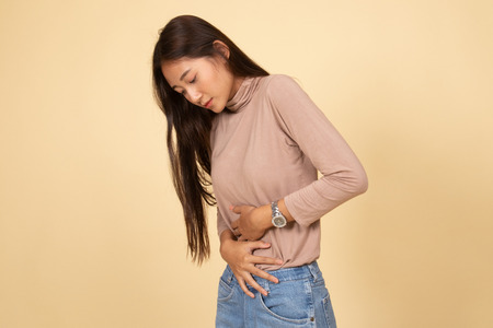 Young Asian woman got stomachache  on beige backgroundの写真素材