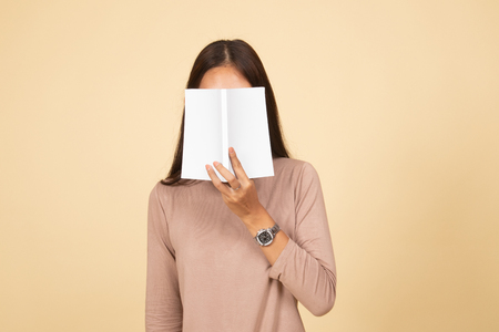 Young Asian woman with a book cover her face  on beige backgroundの写真素材