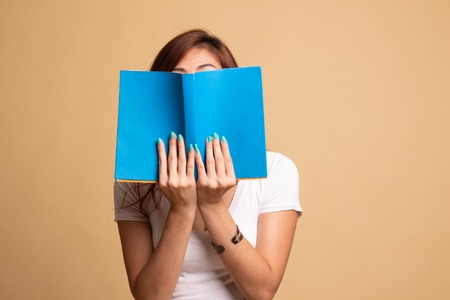 Young Asian woman with a book cover her face on beige background