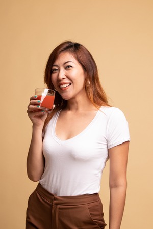 Young Asian woman drink tomato juice on beige backgroundの写真素材