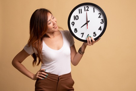 Young Asian woman with a clock on beige backgroundの写真素材