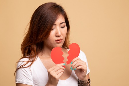 Beautiful young Asian woman with broken heart on beige backgroundの写真素材