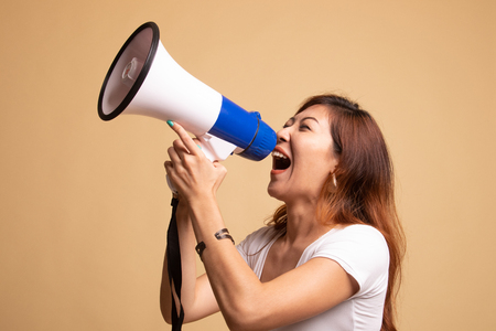 Beautiful young Asian woman announce with megaphone on beige backgroundの写真素材