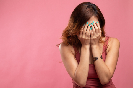 Sad young Asian woman cry with palm to face on pink backgroundの写真素材