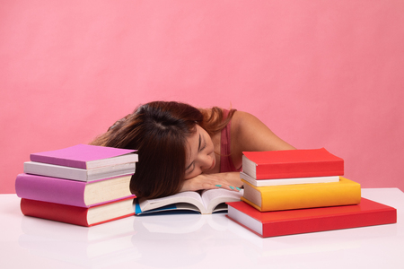 Exhausted Young Asian woman sleep with books on table on pink backgroundの写真素材