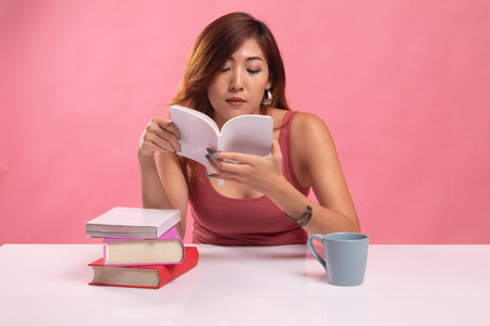 Young Asian woman read a book with cup of coffee on pink backgroundの写真素材