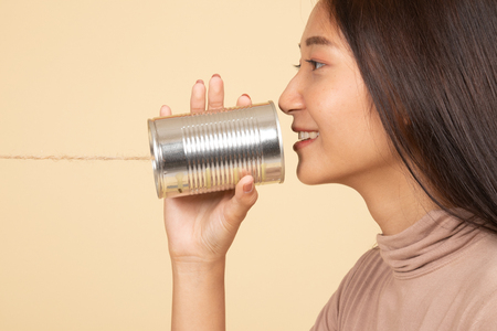 Young Asian woman with tin can phone  on beige backgroundの写真素材
