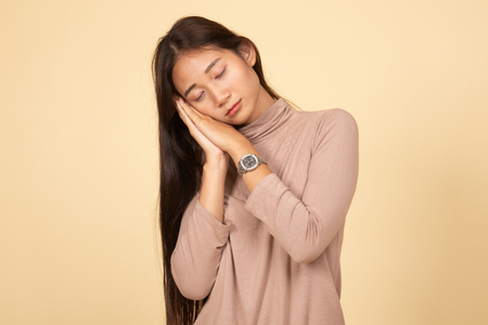Beautiful young Asian woman with sleeping gesture  on beige backgroundの写真素材