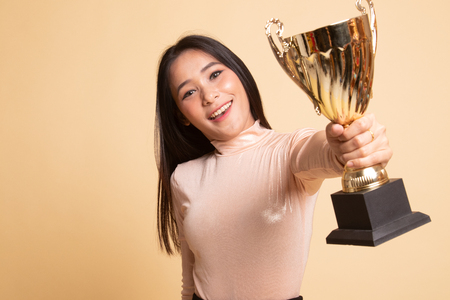 Successful young asian woman holding a trophy on  beige backgroundの写真素材