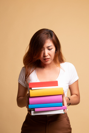Unhappy young Asian woman studying  with may books on beige backgroundの写真素材