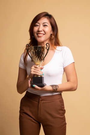 Successful young asian woman holding a trophy on beige backgroundの写真素材