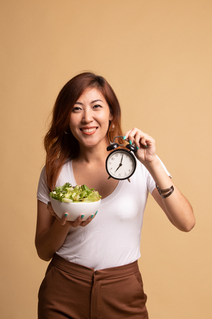 Young Asian woman with clock and salad on beige backgroundの写真素材