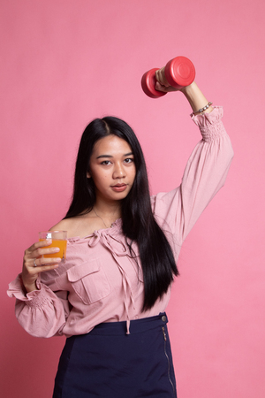 Young Asian woman with dumbbell drink orange juice on pink backgroundの写真素材