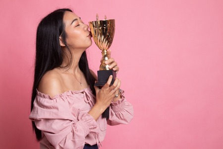 Successful young asian woman holding kissing a trophy on pink backgroundの写真素材