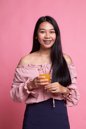 Young Asian woman drink orange juice on pink backgroundの写真素材
