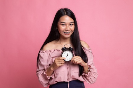 Young Asian woman smile with a clock on pink background