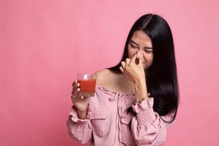 Young Asian woman hate tomato juice on pink backgroundの写真素材