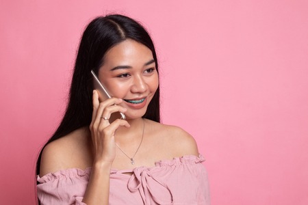 Young Asian woman talking with mobile phone on pink backgroundの写真素材