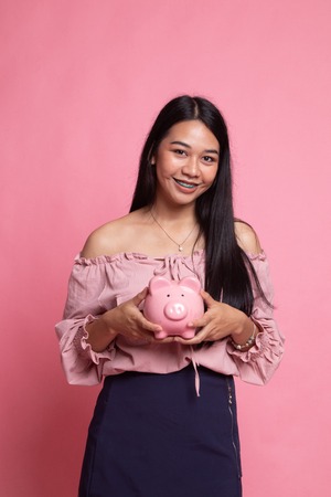 Young Asian woman with a pig coin bank on pink backgroundの写真素材