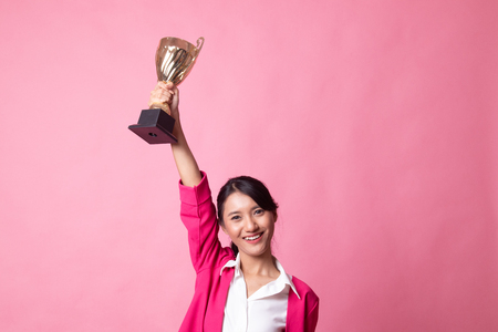 Successful young asian woman holding a trophy on pink backgroundの写真素材