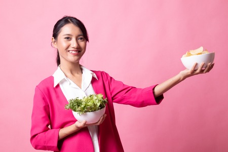 Young Asian woman with potato chips and salad on pink backgroundの写真素材