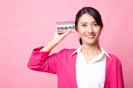 Young Asian woman with tin can phone on pink backgroundの写真素材