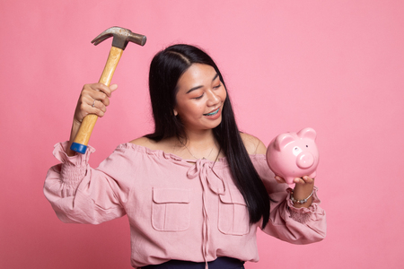 Asian woman with pig coin bank and hammer on pink backgroundの写真素材