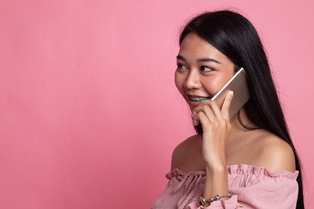 Young Asian woman talking with mobile phone on pink backgroundの写真素材