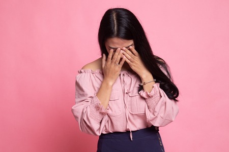 Sad young Asian woman cry with palm to face on pink background