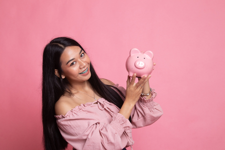 Young Asian woman with a pig coin bank on pink backgroundの写真素材