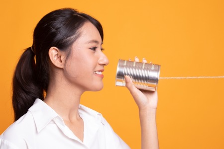 Young Asian woman with tin can phone on yellow backgroundの写真素材