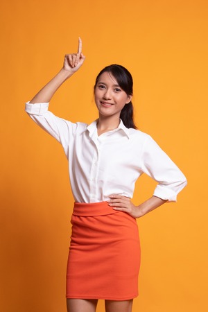 Young Asian woman smile and point up on yellow backgroundの写真素材