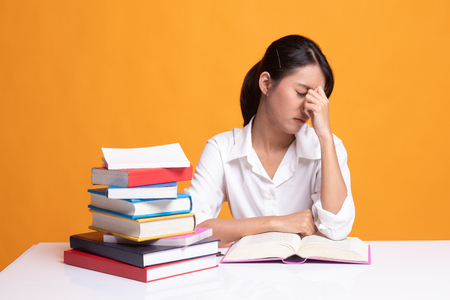 Exhausted Asian woman got headache read a book with books on table on yellow backgroundの写真素材